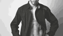 a man is standing in a black and white photo with his shirt open .