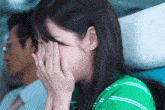 a woman in a green striped shirt covering her face with her hands