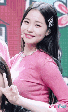 a woman in a pink shirt giving a peace sign with simply pop on the bottom