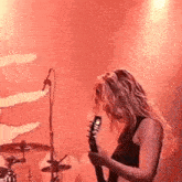 a woman is playing a guitar on a stage in front of a red background .