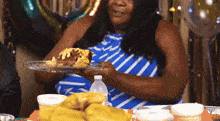 a woman in a blue and white striped dress holds a plate of food in her hands