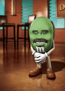 a green m & m with a mustache is kneeling down on the floor .
