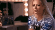 a woman in a sequined shirt is sitting in front of a mirror in a dressing room .