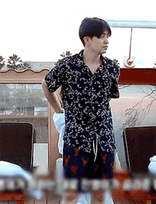 a young man in a floral shirt and shorts is standing in front of a window .
