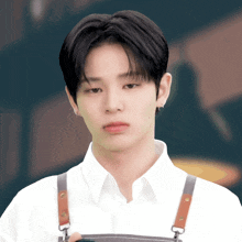a young man wearing an apron and a white shirt looks at the camera