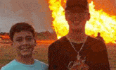 two young men are smiling in front of a large fire .