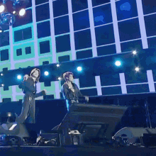 two people singing into microphones on a stage in front of a building