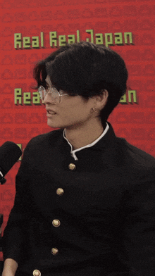 a man wearing glasses is standing in front of a red background that says real real japan
