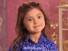a little girl in a blue shirt is making a funny face and saying ohmagawd .
