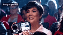 a woman is holding a video camera in front of a crowd of people .