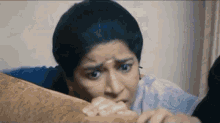 a woman is laying on a couch with her hands on her face and making a funny face .
