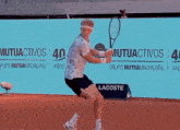 a man is holding a tennis racquet in front of a sign that says lacoste