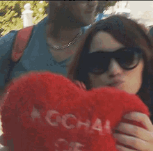 a woman wearing sunglasses is holding a red heart shaped pillow that says kocham
