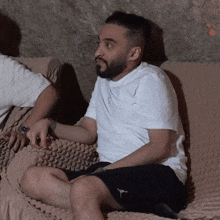 a man sitting on a couch wearing a white shirt and black shorts with the word jordan on them