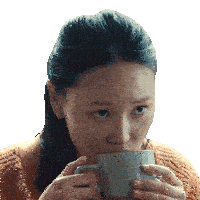 a woman in an orange sweater is drinking from a gray mug