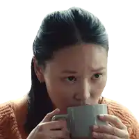 a woman in an orange sweater is drinking from a gray mug