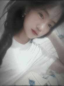 a girl wearing a white t-shirt and earrings looks at the camera