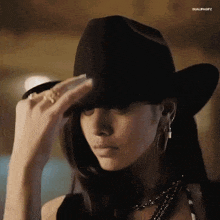 a woman wearing a black cowboy hat is adjusting her hat .