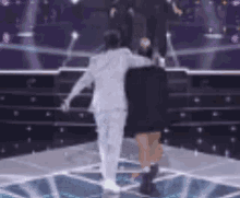 a man in a white suit and a woman in a black dress are walking on a stage .