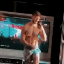 a shirtless man is taking a selfie in front of a television while standing in front of a mirror .