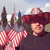a man wearing a cowboy hat is standing in front of a bunch of american flags