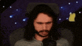 a man with long hair and a beard is sitting in front of a microphone and making a funny face