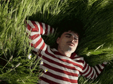 a man wearing a red and white striped shirt is laying in the grass