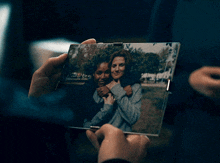 a woman is holding a picture of two women hugging each other