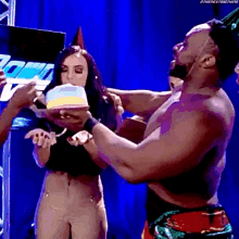 a man is holding a cake in front of a woman who is wearing a party hat ..