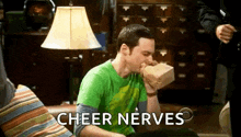 a man in a green shirt is sitting on a couch eating a paper bag .