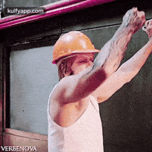 a man wearing a hard hat and a white tank top is holding his fist up .