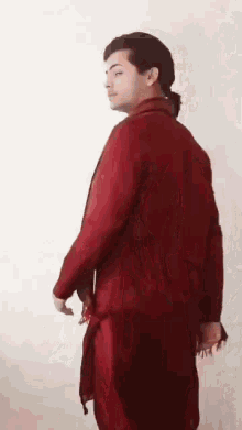 a man in a red suit is standing in front of a white wall and looking at the camera .