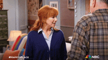 a woman in a blue cardigan is talking to a man in a plaid shirt with the nbc logo in the background
