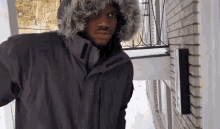 a man wearing a fur hooded jacket is standing in front of a brick building