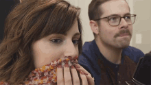 a woman covering her face with a scarf and a man with glasses behind her