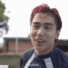 a man with red hair is smiling and wearing a blue shirt .