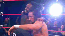 a wrestler is hugging another wrestler in a boxing ring
