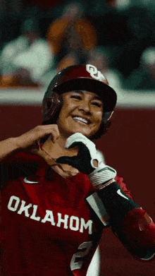 a woman wearing a oklahoma jersey is smiling and making a heart shape with her hands
