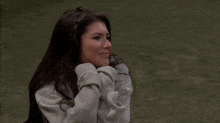 a woman wearing a grey sweatshirt is laughing with her hands on her face