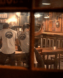 a man wearing a t-shirt with a logo on the back of it is sitting at a table in a restaurant