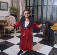 a young boy in a red robe and sunglasses stands in a room with a checkered floor