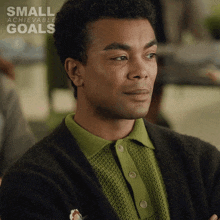 a man wearing a green shirt and a black cardigan with small achievable goals written on the bottom right