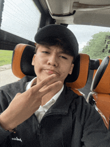 a young man wearing a black jacket and a black hat takes a selfie in a car