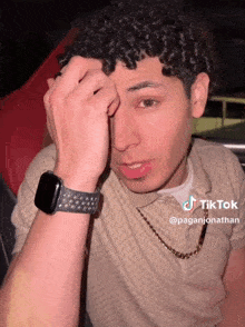 a man with curly hair is wearing a watch and has a tiktok sticker on his face