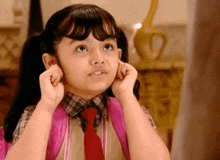 a little girl with pigtails and a pink backpack is covering her ears with her hands .