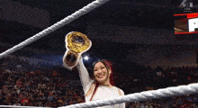 a woman in a wrestling ring holds a gold belt