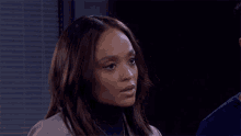 a woman wearing a turtleneck and a jacket looks at the camera with a serious look on her face