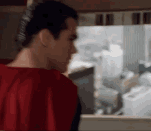 a man in a red cape is standing in front of a window and looking out .