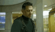 a man wearing a black turtleneck and a backpack is standing in a building .