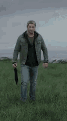 a man is walking through a grassy field with an umbrella .